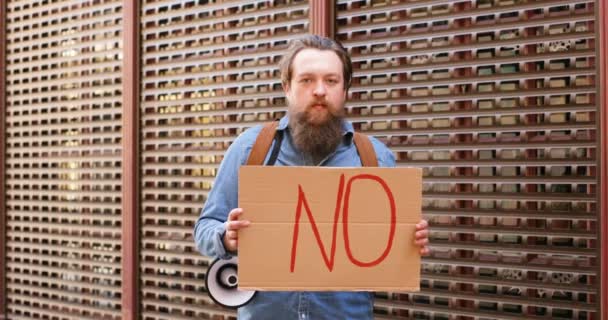 Portraitaufnahme eines jungen Mannes aus dem Kaukasus, der ein Plakat mit der Aufschrift "No" zeigt. Männlicher Aktivist zeigt Tafel mit Protest zu politischen oder ökologischen Themen. Einsam protestierend. Konzept der Verweigerung und Leugnung. — Stockvideo