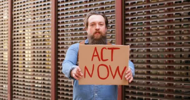 Retrato de tiro do jovem caucasiano demonstrando cartaz com palavras Act Now. Ativista do sexo masculino mostrando quadro com protesto sobre questões políticas ou ambientais. Protesto solitário. Conceito de ativismo . — Vídeo de Stock