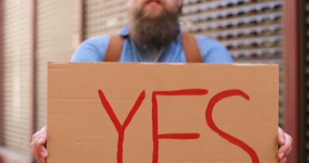 카톤 포스터를 클로즈업하면 Yes 라는 빨간 글자가 튀어나오죠. 실외. 수염을 기른 백인 남자 가 거리에서 카메라 앞에 테이블을 보여 줬어요. 협정 개념. — 비디오