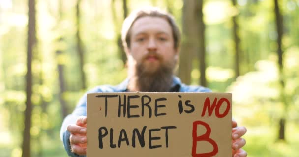 Portrait shot of Caucasian young male eco acivist standing in green forest and rising to camera poster with words There is no planet B. Handsome man protesting for clean and safe environment. Blurred. — Stock Video