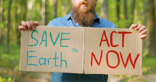 Tutup poster karton dengan kata-kata Simpan Bumi dan Undang-Undang Sekarang di tangan orang Kaukasia. Aktivis eko laki-laki berdiri di hutan atau taman pada hari yang cerah dengan protes tunggal. — Stok Video