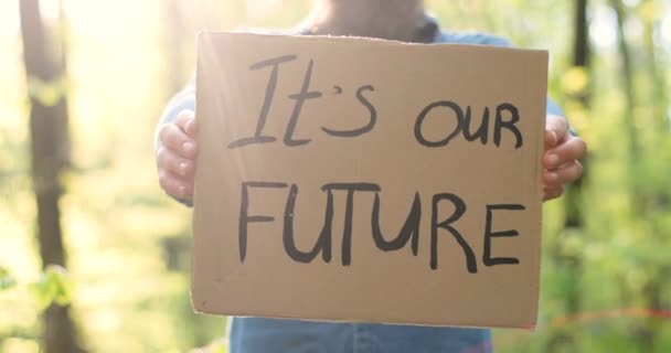 Großaufnahme eines Plakats mit der Aufschrift "Unsere Zukunft in den Händen des kaukasischen Mannes". Männlicher Öko-Aktivist steht an sonnigen Tagen mit einsamem Protest im Wald oder Park. — Stockvideo