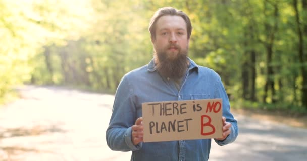 Portret van blanke jonge mannelijke eco-acivist in groen zonnig park en poster met woorden Er is geen planeet B. Er is geen planeet. Knappe man voor schone en veilige natuur. Milieuactivisme. — Stockvideo