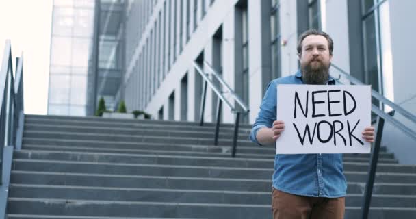 Портрет кавказского безработного молодого человека с бородой, стоящего на улице с объявлением, нуждается в доработке. Мужчина безработный одинокий протестант. Тяжелые времена безработицы после блокировки . — стоковое видео