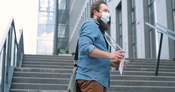 Caucasian young jobless man in medical mask standing outdoor at big stairs and holding carton table with words Need Work. Male demonstrating board with protest against lockdown politics issues. — Stock Video