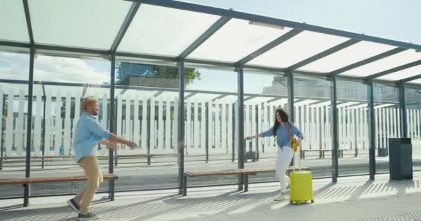 Alegre pareja joven caucásica en el amor encuentro en la estación de tren y abrazos. Tipo girando chica en el día de verano. Feliz hombre guapo conocer a una mujer hermosa en la parada de autobús. Volviendo del viaje. Exterior . — Vídeos de Stock