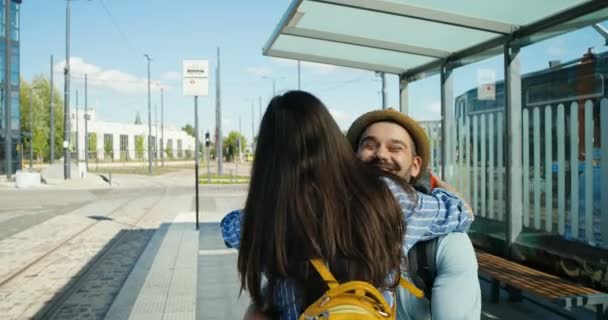 Joyful casal jovem caucasiano no encontro de amor na estação de trem e abraços. Guy girando menina no dia de verão. Homem bonito feliz conhecer mulher bonita na parada de ônibus. Voltando da viagem. Ao ar livre . — Vídeo de Stock