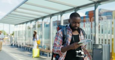 Fotoğraf makinesi ve sırt çantasıyla gezen Afro-Amerikalı genç, yakışıklı bir gezgin. Güzel görünümlü mutlu erkek turist otobüste ve tramvayda geziniyor ve doğru yolu arıyor.