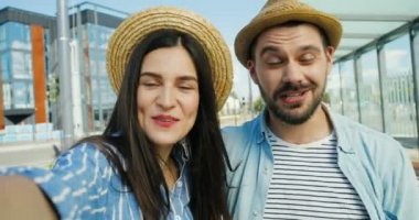 Kafkasyalı genç mutlu turistlerin yakın çekimleri şapkalı bir çift konuşuyor, el sallıyor ve yazın dışarıda kameralara gülümsüyor. Erkek ve kadın gezginlerin video kaset taktıkları pov. Video sohbet konsepti.