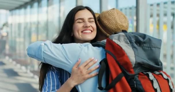 Bella giovane donna bruna caucasica che sorride e incontra fidanzato o marito all'aperto alla fermata dell'autobus. Tornare a casa dopo il viaggio. Una coppia innamorata si incontra. Indietro vista di ragazzo viaggiatore abbracciare fidanzata. — Video Stock