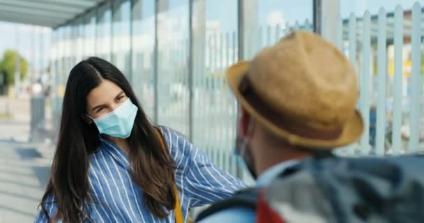 Caucasian young woman meeting boyfriend or husband outdoors. Coming back home from travel. Couple in medical masks meet. Back view of guy traveller hugging girlfriend. Coronavirus pandemic. — Stock Video