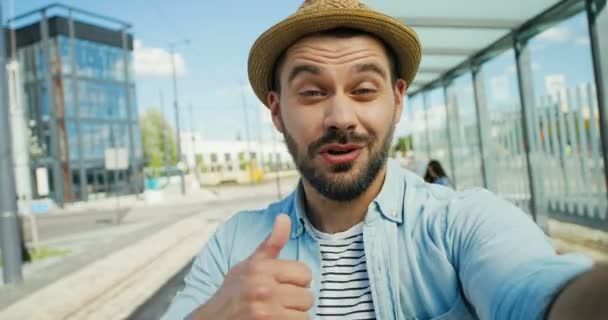 Close up de caucasiano jovem turista feliz em chapéu falando, dando polegar para cima e sorrindo para câmera ao ar livre no verão. POV de belo homem viajante com barba tendo videochat. Conceito de Videochat — Vídeo de Stock