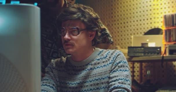 Caucasian young man technician of 80s in glasses and with mustache working at vintage computer monitor, searching for information, talking with colleague. Style of 70s. Males retro hackers in smoke. — Stock Video