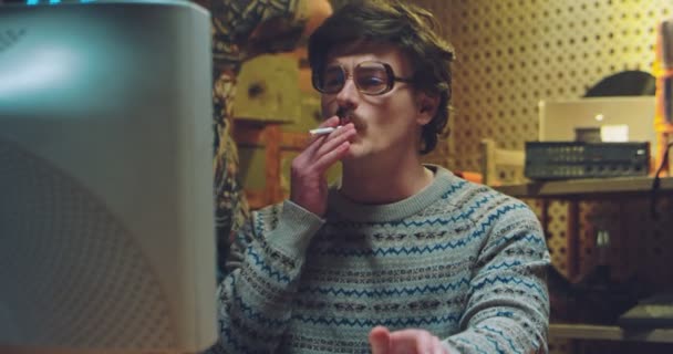 Homem caucasiano de óculos, estilo retro com bigode fumando cigarro no monitor vintage do PC no quarto dos anos 80 e conversando com colega. Hackers masculinos dos anos 70 trabalhando no computador com disquetes. — Vídeo de Stock