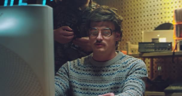 Retro hímek hackerek beszélgetnek a kis szobában, és régi számítógépen dolgoznak. 80-as évekbeli fehér férfi szemüvegben és bajusszal a monitor előtt cigarettázik. 70-es évekbeli munkatárs technikusok. — Stock videók