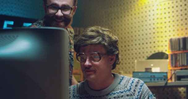 Två kaukasiska hannördar framför PC-monitorn och tittar på något. Vintage70-tals stil. Retro män tekniker eller hackare som arbetar och ler mot datorn på 80-talet. Inomhus. — Stockvideo