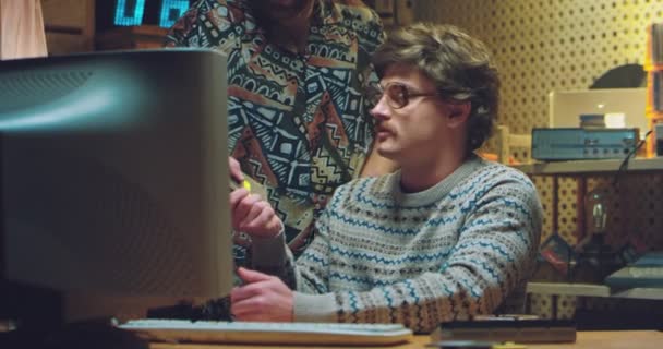 Vit man nörd i glasögon och med mustascher från 70-talet sitter på PC monitor och diskuterar diskett med vän. Hanar hackare på dator gräla och prata hemma i retro interiör. — Stockvideo