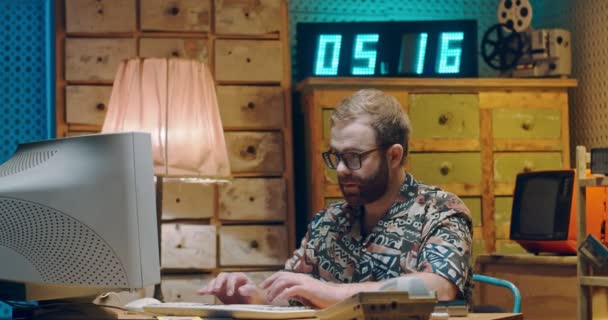 Hvid flot ung mand i briller og farverig skjorte sidder i retro værelse på pc-skærm og skrive på tastaturet. Mand, der arbejder på computer. Vintage stil af hacker. – Stock-video