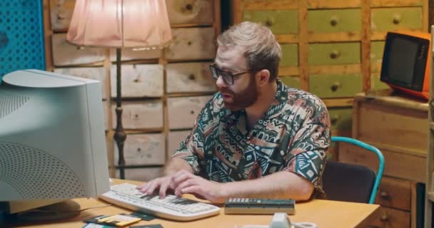 眼鏡をかけた白人ハンサムな男が机の上に座り、古いコンピュータのキーボードを入力します。レトロなインテリア。ヴィンテージスタイル。80年代にPCで働く男性ジャーナリストや作家. — ストック動画