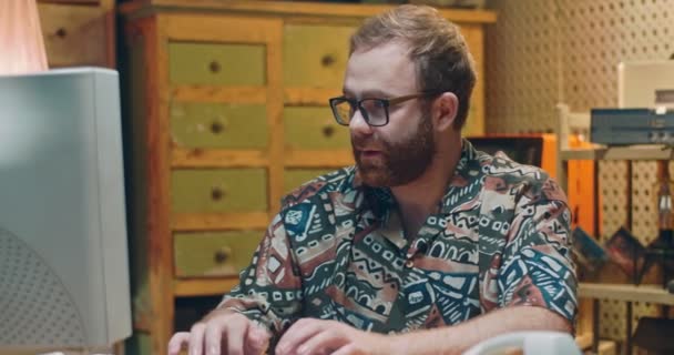 Blanke jongeman in bril en kleurrijk shirt typen op toetsenbord tijdens het werken op de oude computer. Portret van oude retro mannelijke programmeur die glimlacht naar de camera en duim opgeeft. Vintage stijl. — Stockvideo