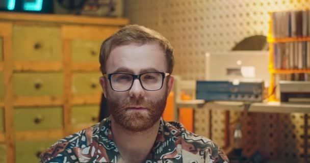 Retrato de jovem caucasiano em óculos olhando em linha reta demais câmera com tristes olhos astutos em estilo vintage. Interior retrô. Close up de nerd masculino com rosto grave chateado. — Vídeo de Stock