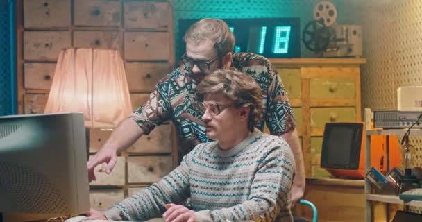 Dos hombres caucásicos amigos nerds de los 80 trabajando y hablando en el viejo monitor de PC. Hombres divertidos hackers o programadores de los años 70 discutiendo algo en la computadora. — Vídeo de stock