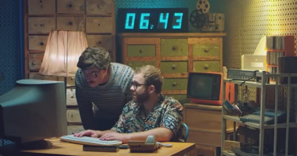 Two Caucasian males programists in glasses and funny looks working at PC monitor and talking when deciding some problem. Retro style of 80s. Vintage computer. Men nerds of 70s. Help from friend. — Stock Video