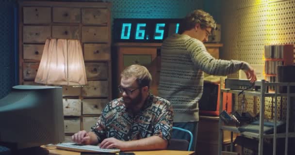 Caucasian young man in glasses working at old computer. Male colleague talking on wired vintage telephone behind and is cheerful. Retro concept. Males nerds programists of 80s. Successful phone call. — Stock Video