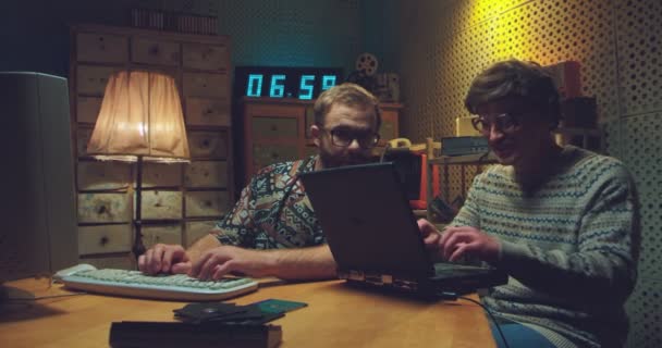 Kaukasische männliche Nerds sitzen am Schreibtisch, reden und arbeiten am Computer. Zwei Retro-Männer tippen auf Tastaturen, studieren und zeigen Bildschirme mit Arbeit. Vintage-Stil der 90er Jahre. Freunde der 80er Jahre. — Stockvideo