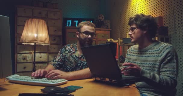 Καυκάσιοι άντρες σπασίκλες κάθονται στο τραπέζι, μιλάνε και δουλεύουν σε υπολογιστές. Δύο ρετρό νέοι προγραμματιστές δακτυλογραφούν σε πληκτρολόγια, μελετούν και κοροϊδεύουν. Vintage στυλ του '90. Φίλοι της δεκαετίας του 80. — Αρχείο Βίντεο