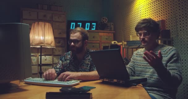 Caucásico hombres nerds estudiantes sentados en el escritorio, hablando y trabajando en computadoras. Dos jóvenes retro programadores estudiando y peleando. Estilo vintage de los 90. Amigos de los 80. Chicos disputando. — Vídeo de stock