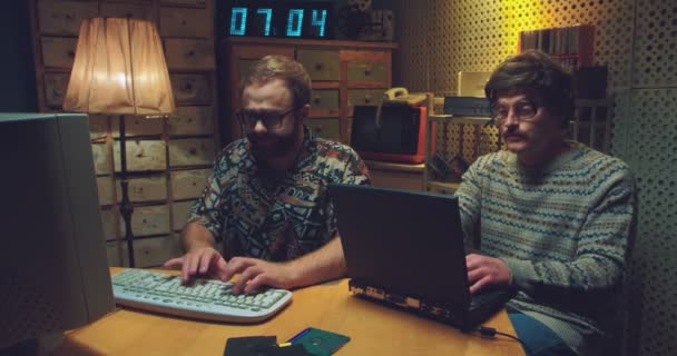 Blanke mannen nerds zitten aan tafel, praten en werken aan computers. Twee retro jonge mannen programmeurs typen op toetsenborden, studeren en bespotten. Vintage stijl van de jaren 90. Vrienden hackers van 80s. — Stockvideo