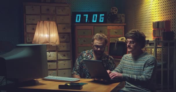 Hombres caucásicos nerds sentados en el escritorio, hablando y trabajando en computadoras. Dos programadores retro hombres escribiendo en teclados, estudiando y codificando. Estilo vintage de los 90. Amigos hackers de los años 80. — Vídeo de stock