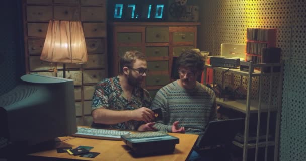 Hombres caucásicos nerds sentados en el escritorio, hablando y trabajando en la computadora con disquete. Programadores de hombres retro escribiendo en el teclado, estudiando, contando con calculadora antigua. Vintage de los 70. Hackers de los 80 — Vídeo de stock