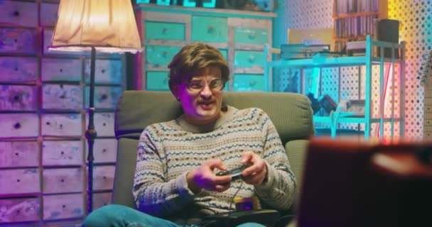 Caucasian man nerd in glasses and with mustache sitting in front of vintage TV monitor and playing videogame with joystick. Male silly goofy loosing in game. Retro style of 80s. Gamer loser from 90s — Stock Video