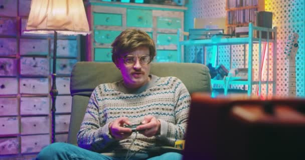 Homme caucasien nerd dans des lunettes et avec moustache assis devant un écran de télévision vintage et jouer au jeu vidéo avec joystick. Homme stupide fou gagner dans le jeu. Style rétro des années 80. Gamer vainqueur des années 90 — Video