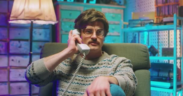Vit ung man nörd i glasögon och med mustasch sitter i retro stil hem och talar på fast vintage telefon på 80-talet. Arg stressad man talar i telefon medan du ringer. Knäppskalle från 90-talet — Stockvideo