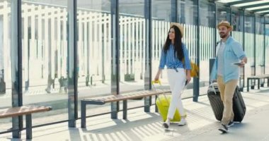 Beyaz, genç, şık, mutlu bir çift otobüs durağında yürüyen ve tekerlekli bavul taşıyan gezginler. Yakışıklı erkek ve güzel kadın, turistler tren istasyonundan ya da havaalanından dışarı çıkıyorlar..