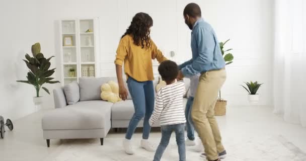 Feliz alegre familia afroamericana bailando y divirtiéndose en la sala de estar en casa durante el encierro. Madre y padre bailan con su pequeño y lindo hijo y su hija. Niños pequeños disfrutando de la música con sus padres. — Vídeos de Stock