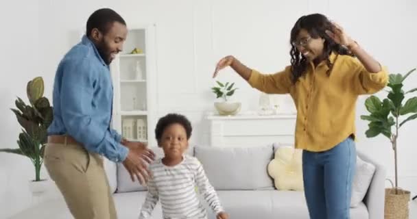 Fröhlich fröhliche afroamerikanische Mutter und Vater tanzen und haben Spaß mit Tochter im Wohnzimmer zu Hause. Familientanz mit kleinen süßen Kindern und Lachen. Kleines fröhliches Kind genießt Musik. — Stockvideo