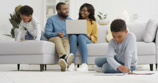 Pequeños niños afroamericanos lindos jugando y pintando cuadros con los padres en acogedora sala de estar. Padres dibujando con su hijo y su hija en casa. Familia pasar tiempo juntos. — Vídeos de Stock