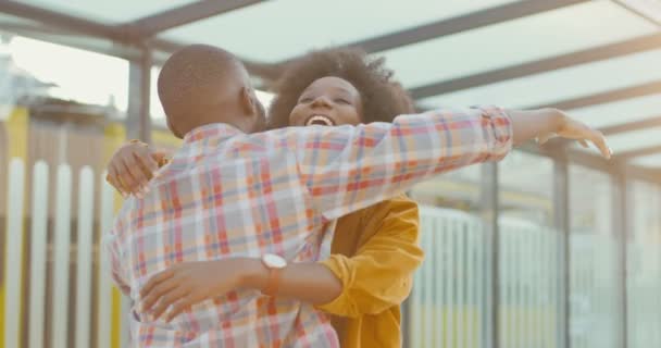 Jovem afro-americana bonita sorrindo e conhecendo namorado ou marido ao ar livre na parada de ônibus. Voltando para casa das viagens. Casal apaixonado conhecer. Vista traseira. cara abraçando namorada e falando. — Vídeo de Stock