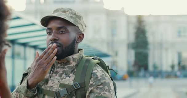 Afroameričan mladý pohledný muž voják ve vojenské uniformě a čepice říkat sbohem a posílání polibky na přítelkyni. Muž jde do armády. Venkovní. Guy a dívka sbohem. — Stock video