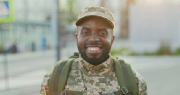 Portretfoto van vrolijke knappe Afro-Amerikaanse jonge mannelijke soldaat in pet met rugzak glimlachend naar camera op straat. Close-up van de man militairen met een glimlach buiten. Militair uniform. Naar het leger gaan. — Stockvideo