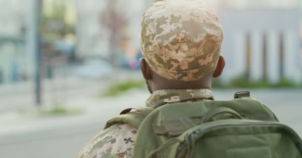 Achter Afro-Amerikaanse jonge mannelijke soldaat in uniform, hoed en met rugzak wandelen buiten. Achteraanzicht op militairen die door de straat lopen in militaire kleding. Naar het leger gaan. — Stockvideo