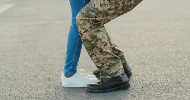 Close-up van de mannelijke en vrouwelijke benen op de weg. Een soldaat in militair uniform die een vriendin of vrouw ontmoet en opheft. Gelukkige ontmoeting van geliefden concept. Man komt terug uit het leger. — Stockvideo