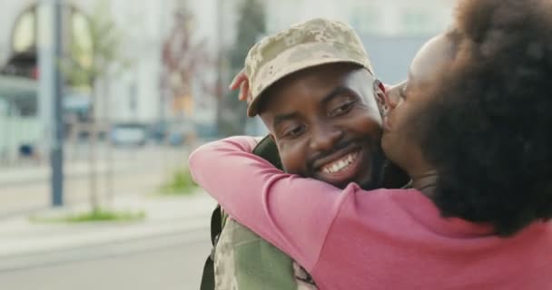 Afro-americano giovane bel soldato maschio in uniforme tornare a casa e incontrare fidanzata piuttosto felice. Uomo in abiti militari abbracciare e abbracciare bella ragazza all'aperto. Chiudete. Posteriore. — Video Stock