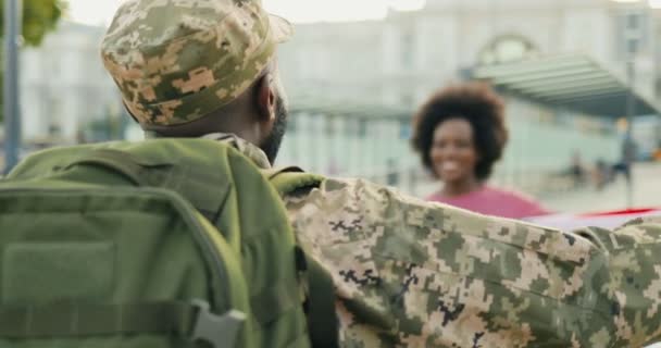 Felice giovane coppia afroamericana incontro e abbraccio in strada. Bello il soldato maschio in uniforme che torna dall'esercito e incontra la bella fidanzata con bandiera USA. Servizio di guerra di ritorno. — Video Stock