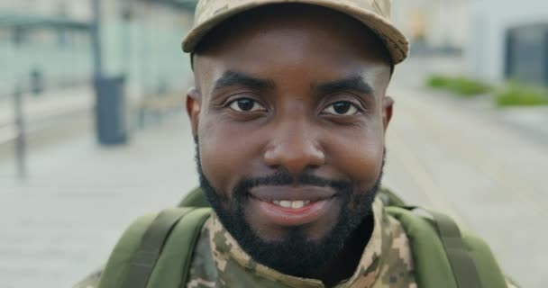 Portret van vrolijke Afro-Amerikaanse knappe jonge mannelijke soldaat in pet met rugzak glimlachend op straat. Close-up van de man militairen met een vrolijke glimlach in de buitenlucht in de stad. Militair uniform. — Stockvideo