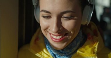 Kulaklık takmış, burnunda piercingler olan neşeli bir şekilde gülümseyen ve müzik dinleyen güzel beyaz bir kız. Güneşli bir sabahta tramvayda ya da otobüste pencerede oturan kadın..